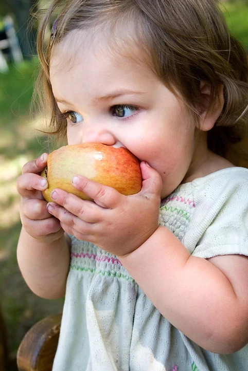 young girl biting into an apple which is a food that's good for your teeth