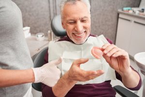 patient in dental chair holding denture after restorative dentistry