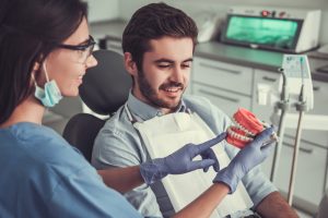 dentist showing patient model of teeth before dental implant treatment