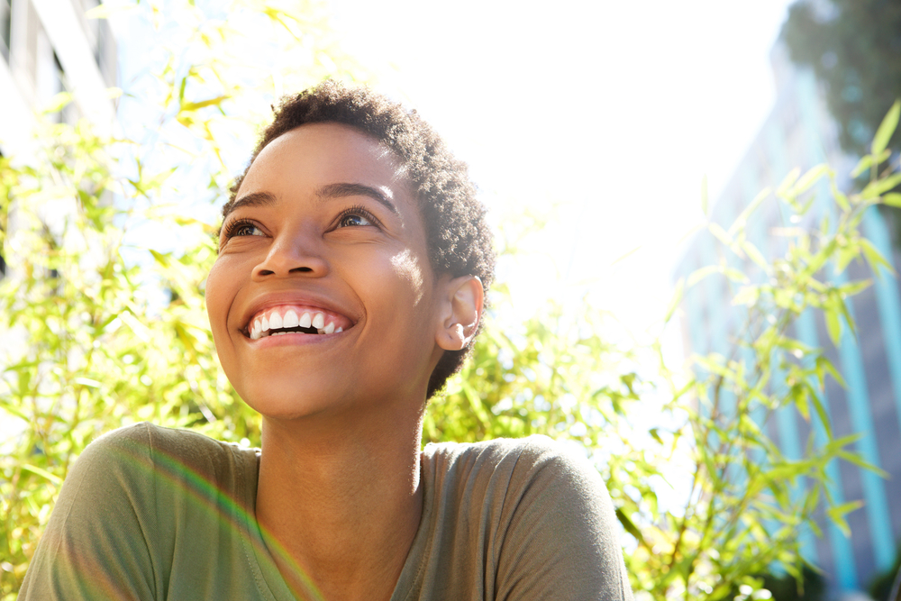 A woman sits outside, smiling about the results of professional teeth whitening.